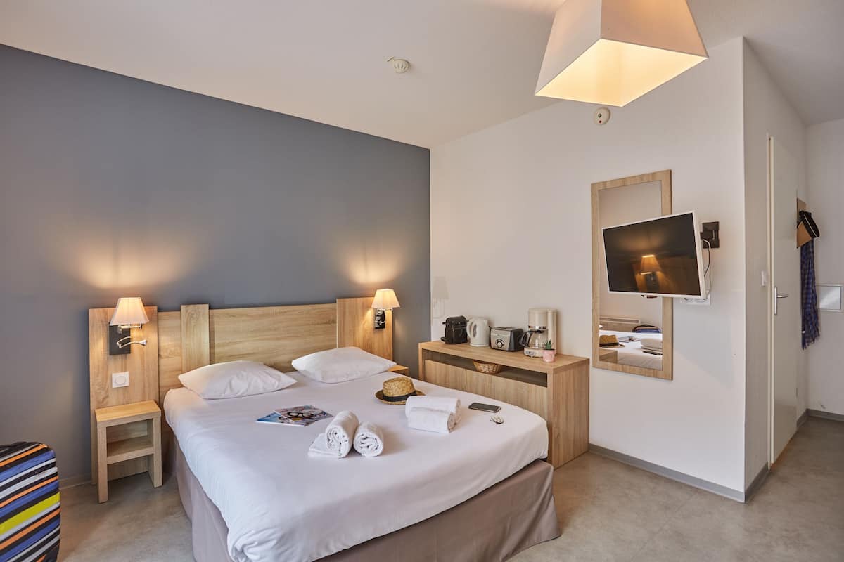 Ett hotellrum med en stor säng, två sängbord med lampor, ett litet bord vid sängen, ett skrivbord med en spegel, en tv och en garderob.
