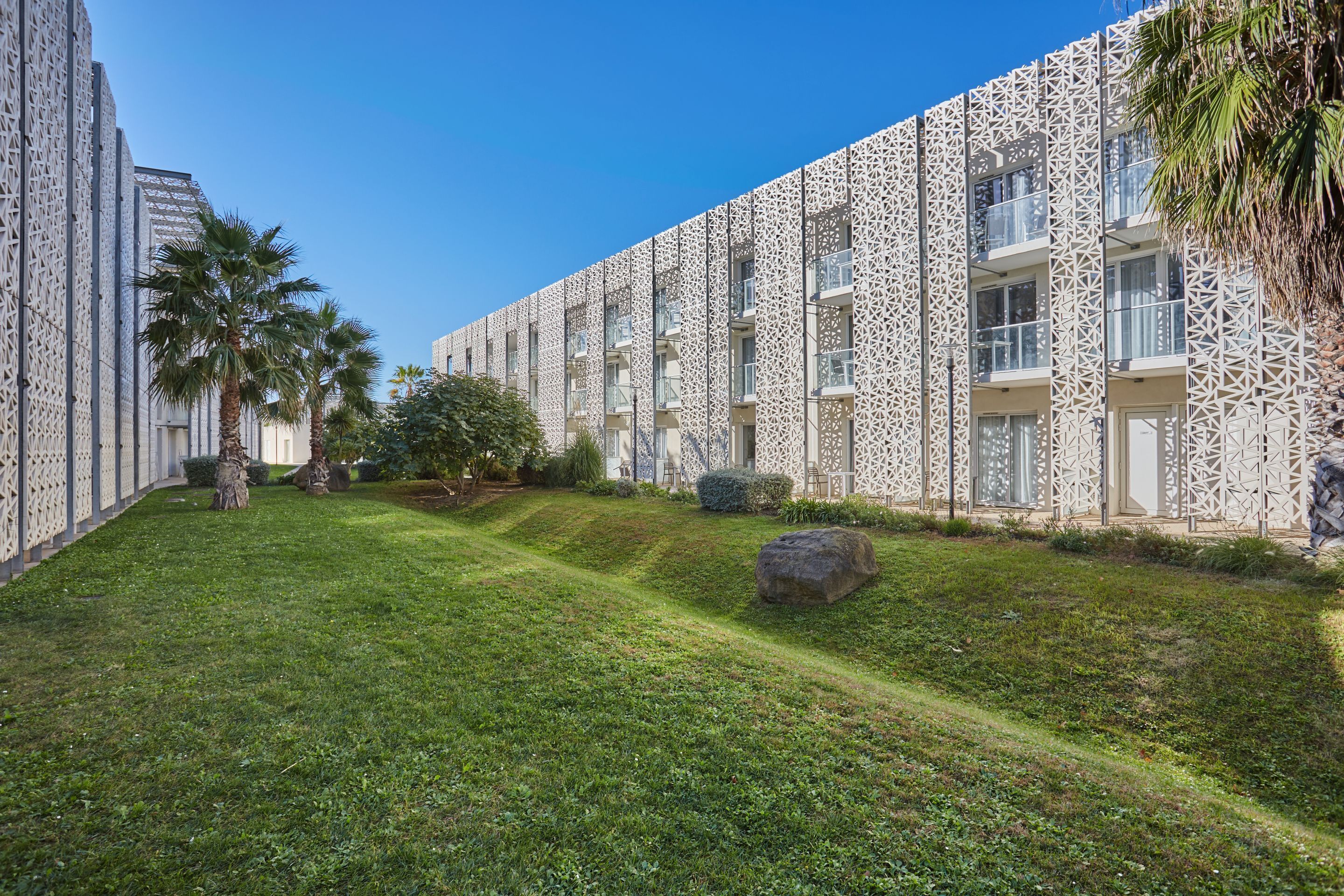 A modern building with patterned exterior walls, a well-maintained lawn, and a palm tree.