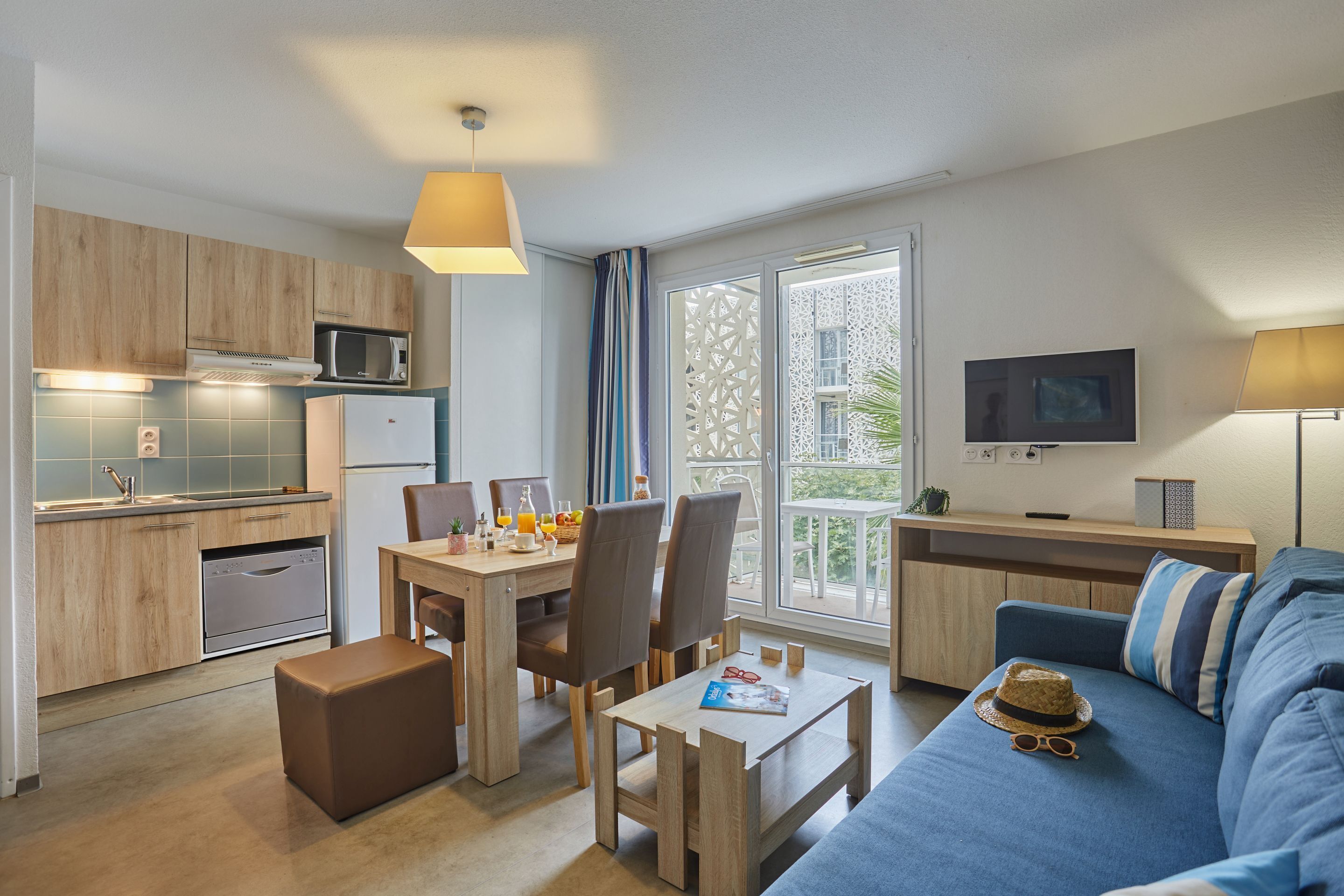 A modern apartment with a kitchen, dining area, and living room. It includes a dining table with chairs, a sofa, a coffee table, and a TV.