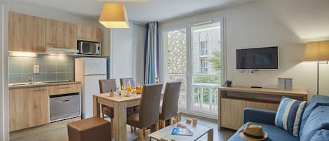 Un appartement moderne comprenant une cuisine, un coin repas et un salon. Il est équipé d’une table à manger avec des chaises, d’un canapé, d’une table basse et d’un téléviseur.