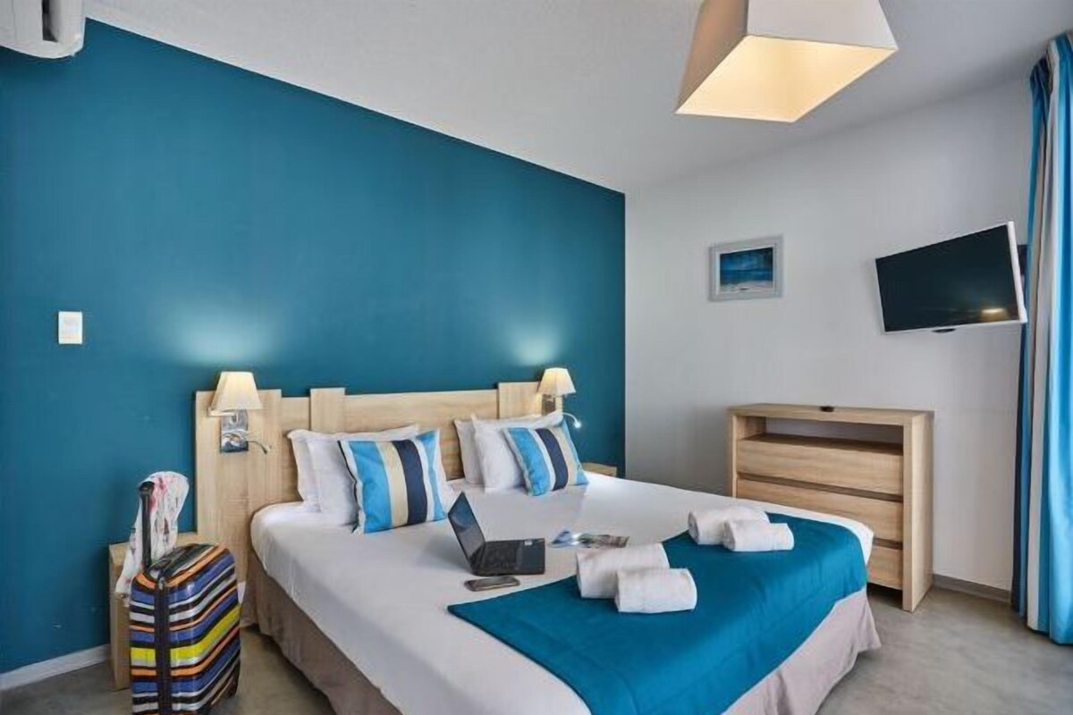 Une chambre d’hôtel avec un lit, un bureau, une télévision et une valise.