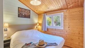 A cozy room with wooden walls, a large bed, two bedside lamps, a window with curtains, and a wall-mounted picture. - Résidence Odalys Shangri-La - Les Hauts de Cassis (Carnoux-en-Provence)