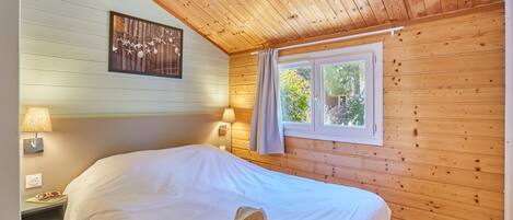 Una habitación acogedora con paredes de madera, una cama grande, dos lámparas de noche, un ventanal con cortinas y un cuadro colgado en la pared.