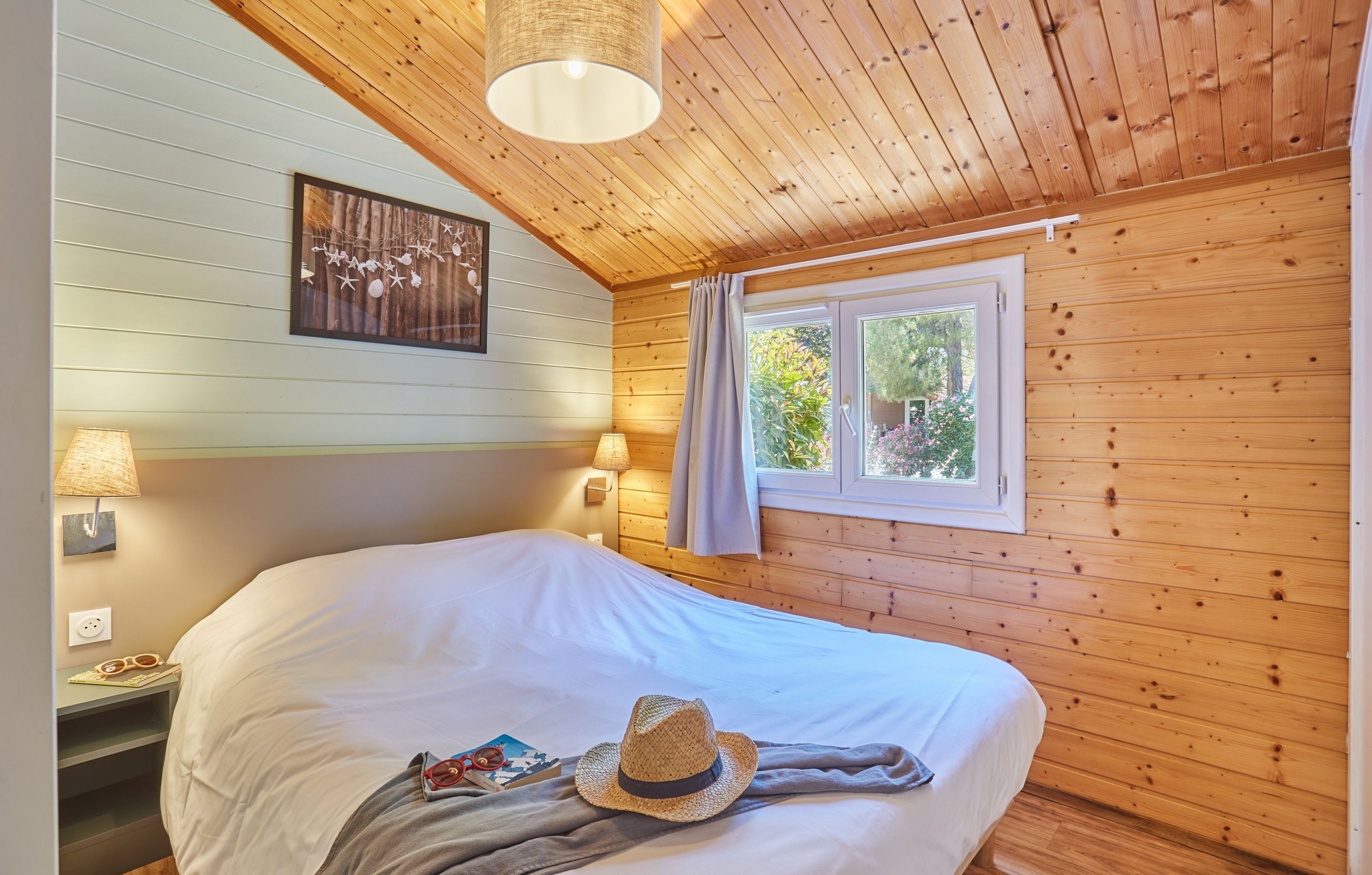 Una camera accogliente con pareti in legno, un letto grande, due lampade sui comodini, una finestra con tende e un quadro appeso al muro.