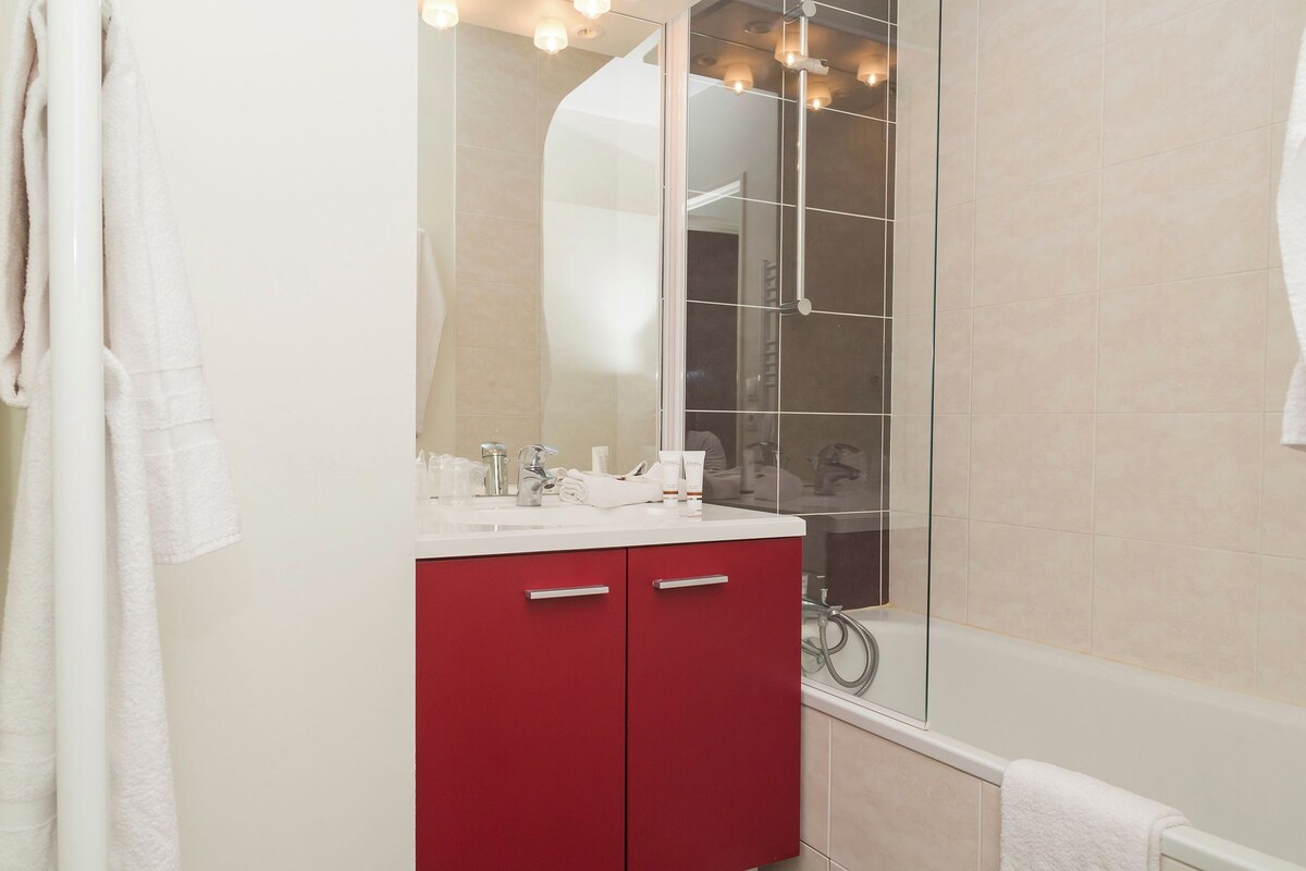 A bathroom with a glass shower enclosure, a red vanity, and a white bathtub.