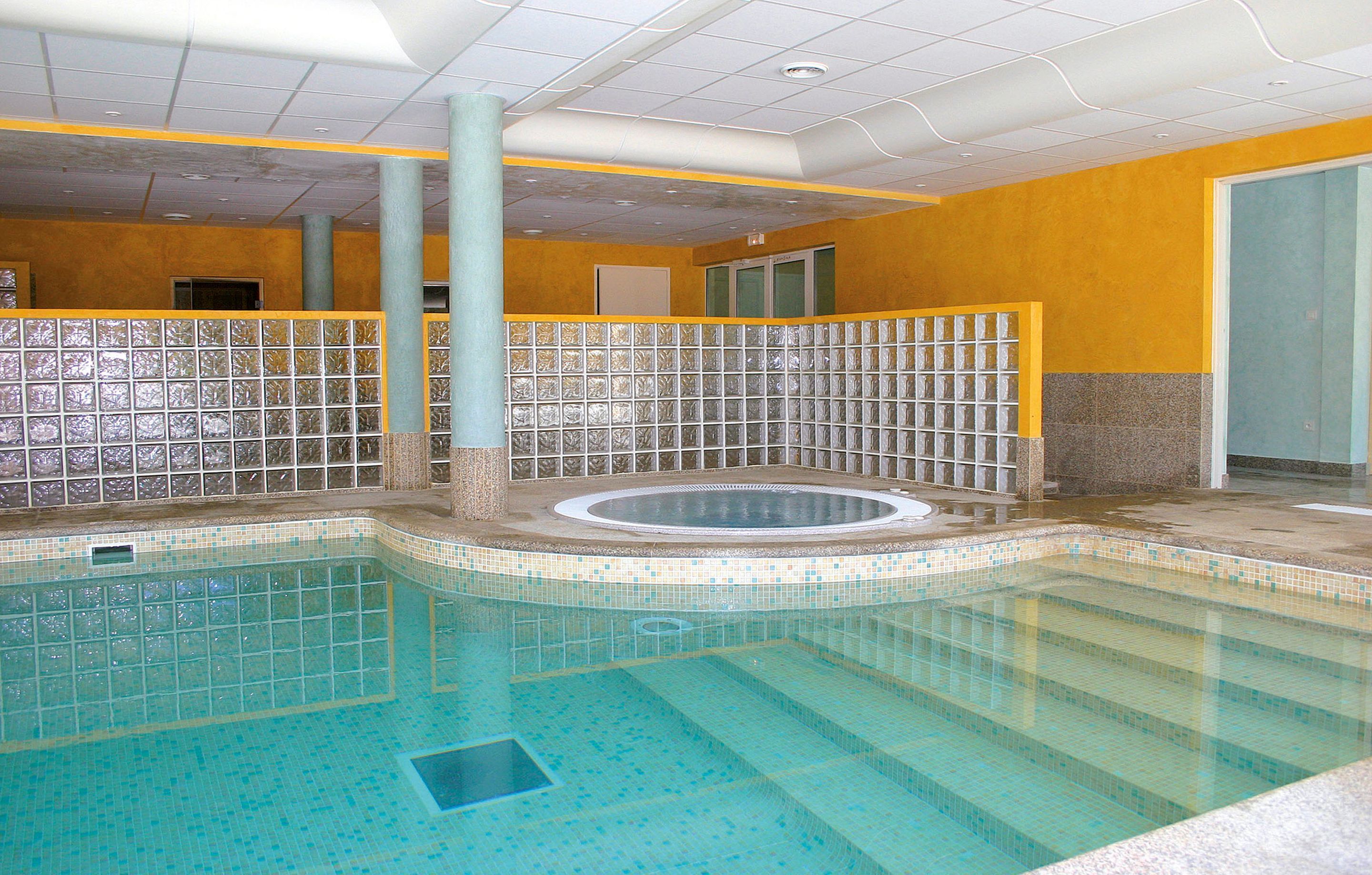 Una piscina interior con paredes de azulejos y una zona de hidromasaje en el centro.