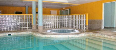 An indoor swimming pool with tiled walls and a central hot tub area.