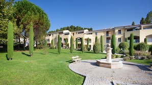 A courtyard with a fountain, neatly trimmed hedges, and a row of buildings with balconies.