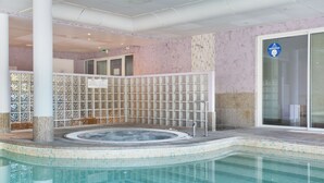 A swimming pool with a hot tub, tiled walls, and a glass door.