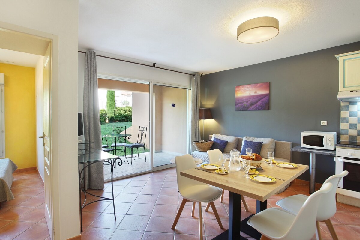 Comedor con mesa dispuesta para cuatro, cocina con microondas y vista a un jardín por una puerta corredera.