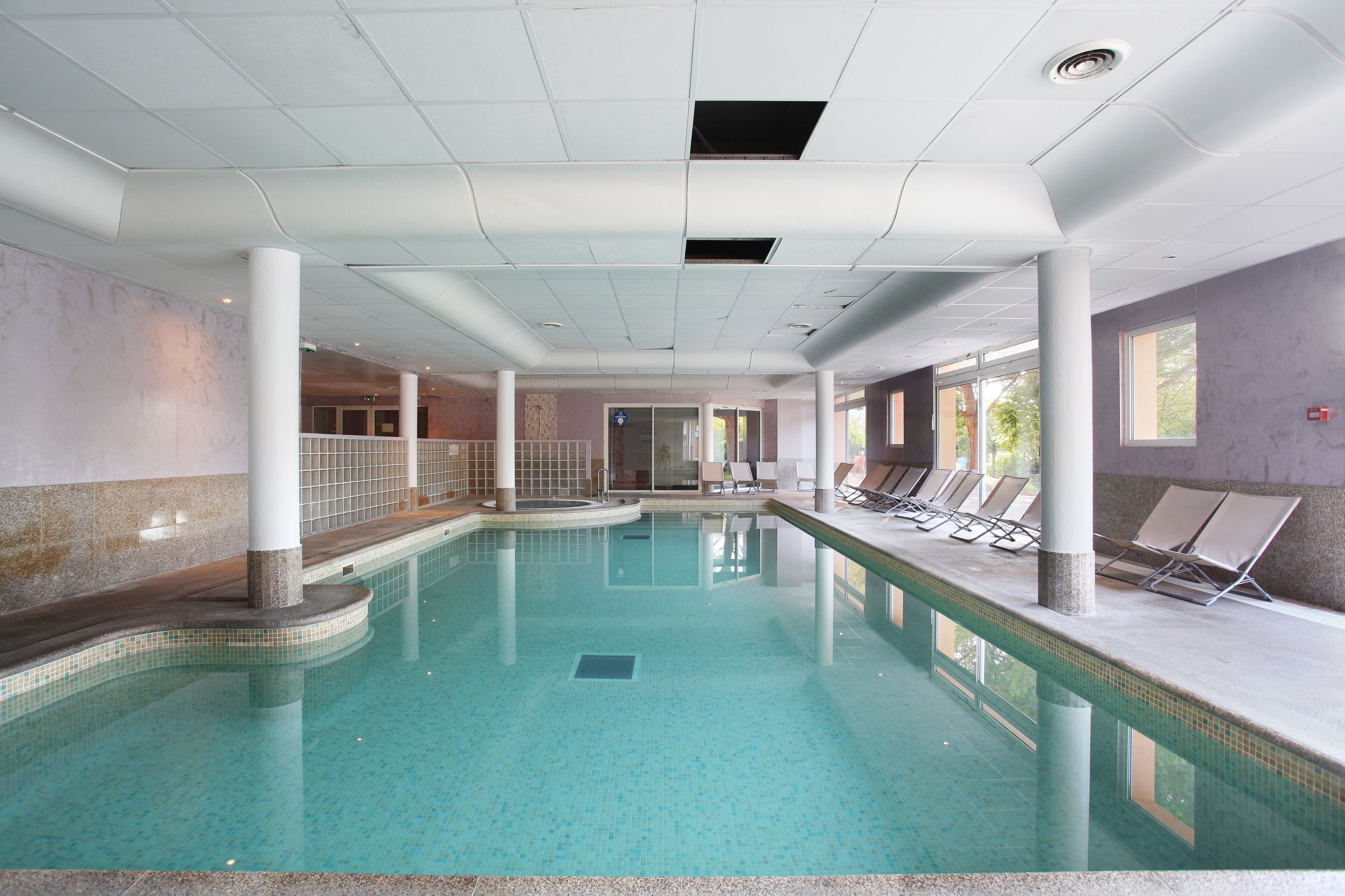 Une piscine intérieure à l’eau claire, entourée de chaises longues et dotée d’un sol carrelé.