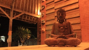 Eine Statue einer sitzenden Figur in meditativer Pose auf einer Holzplattform.