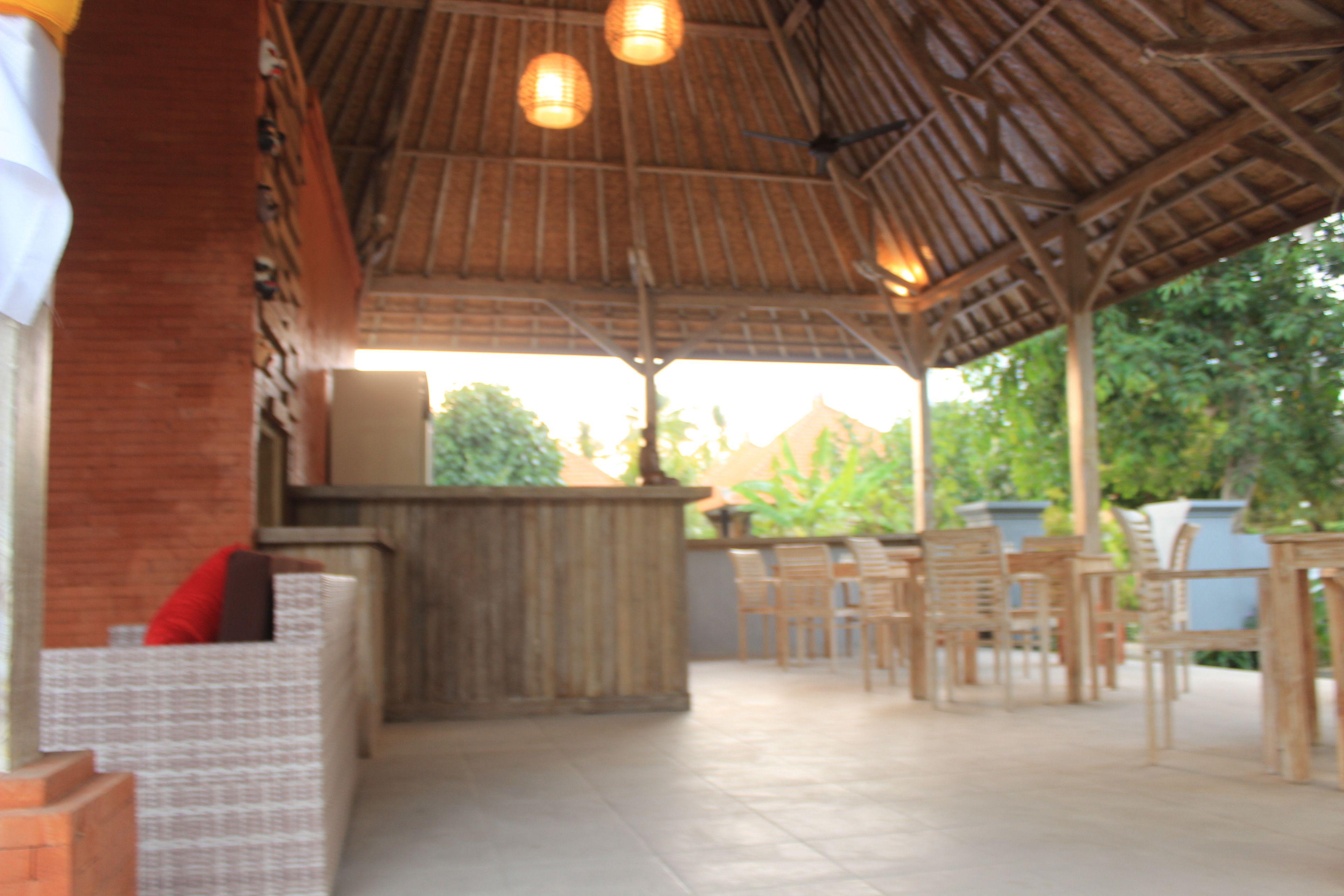 An outdoor patio area with a thatched roof, wooden furniture, and a bar counter.
