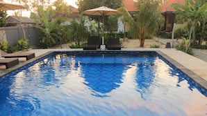 Ein rechteckiger Pool mit Fliesenbord, umgeben von einer Terrasse mit Liegestühlen und einem großen Sonnenschirm.