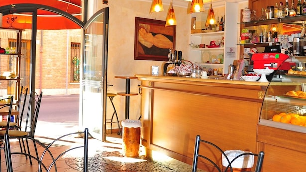 A cozy cafe with exposed wooden beams, a bar area with various drinks and pastries, and a seating area with chairs and a table. - Locanda Modigliani (Ferrara)