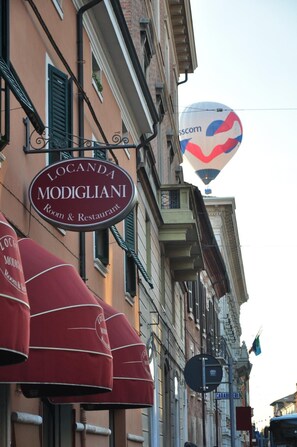 Un edificio con un letrero que dice "Locanda Modigliani Room & Restaurant" y toldos rojos.