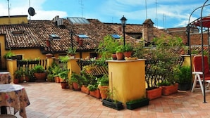 An outdoor patio area with terracotta-tiled flooring, potted plants, and outdoor seating. - Locanda Modigliani (Ferrara)