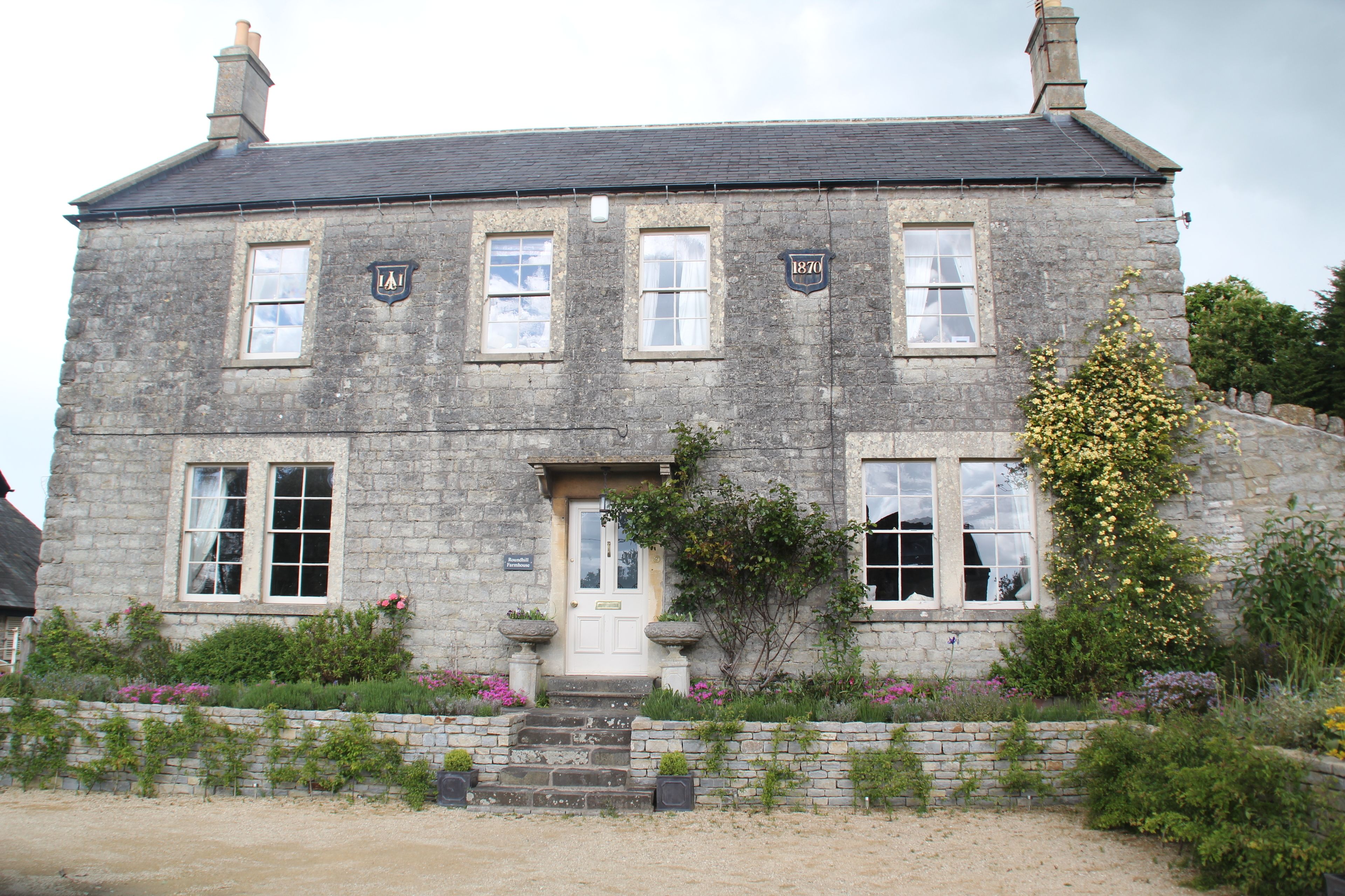 A stone building with a traditional design, featuring a front door, multiple windows, and a small garden area with flowers and plants.