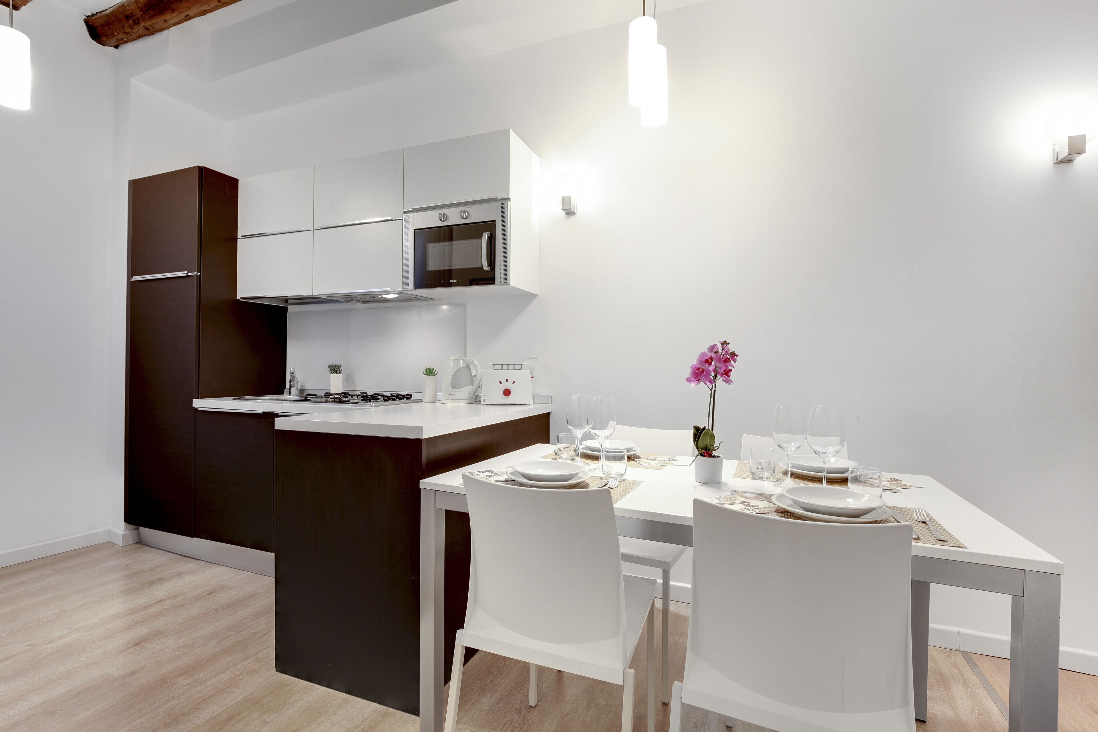 A modern kitchen with white cabinetry and a central island, a dining table set with white chairs, and a small potted orchid on the table.