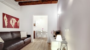 A modern living room with a dark brown leather sofa, a white dining table with chairs, and a white console table with a lamp and decorative items.