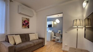 Una sala de estar con un sofá marrón, un comedor con mesa y sillas, y una cocina al fondo.