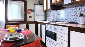 Una cocina con vigas de madera, armarios blancos, una mesa roja y una ventana con cortinas.