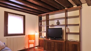 Una sala de estar con un mueble de televisión de madera, un sofá, un radiador y una ventana con cortinas.