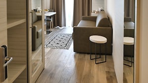 A modern hotel room with a wooden floor, a sofa, a small table, and a mirror. - Hotel Giardinetto (Garda)