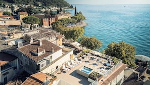 A rooftop terrace with a swimming pool, overlooking a coastal town with terracotta-roofed buildings and a clear view of the sea. - Hotel Giardinetto (Garda)