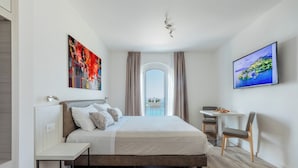 A modern hotel room with a large bed, a desk, a chair, and a TV on the wall. - Hotel Giardinetto (Garda)
