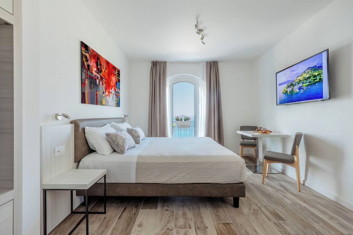 A modern hotel room with a large bed, a desk, a chair, and a TV on the wall.