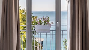 A bedroom with a large arched window overlooking a balcony with a view of the sea. - Hotel Giardinetto (Garda)
