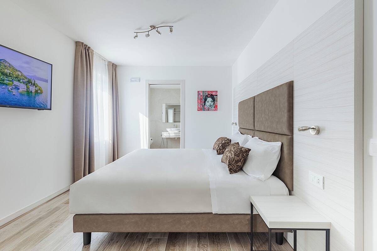 A modern hotel room with a large bed, a bedside table, and a TV mounted on the wall.