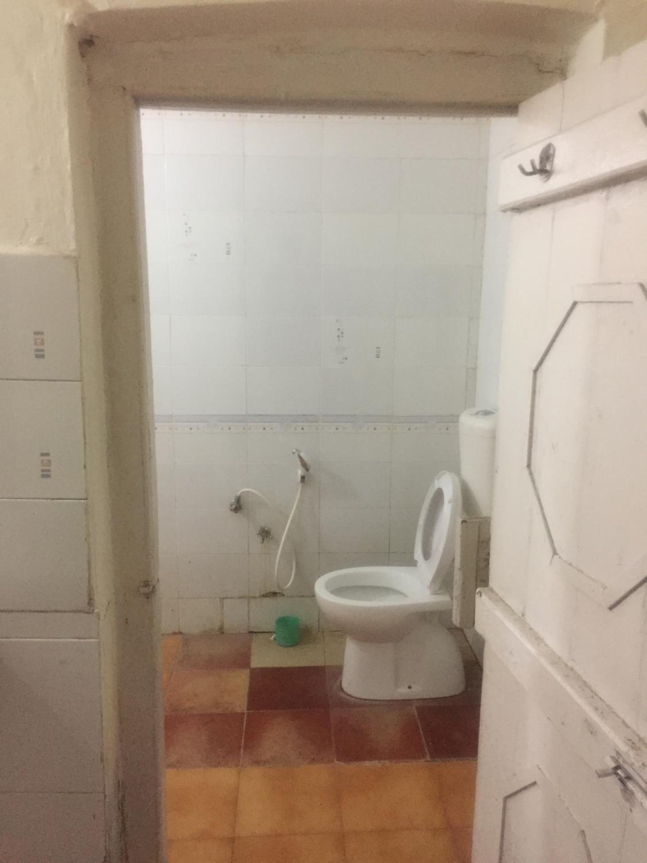 A small, tiled bathroom with a toilet, a shower, and a green trash bin.