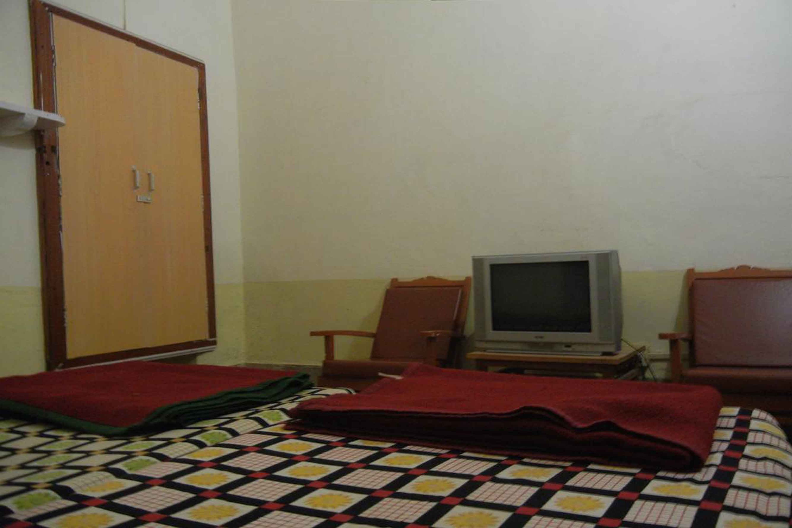Ein Zimmer mit einem Bett, einem Fernseher, einem Kleiderschrank und zwei Sesseln.