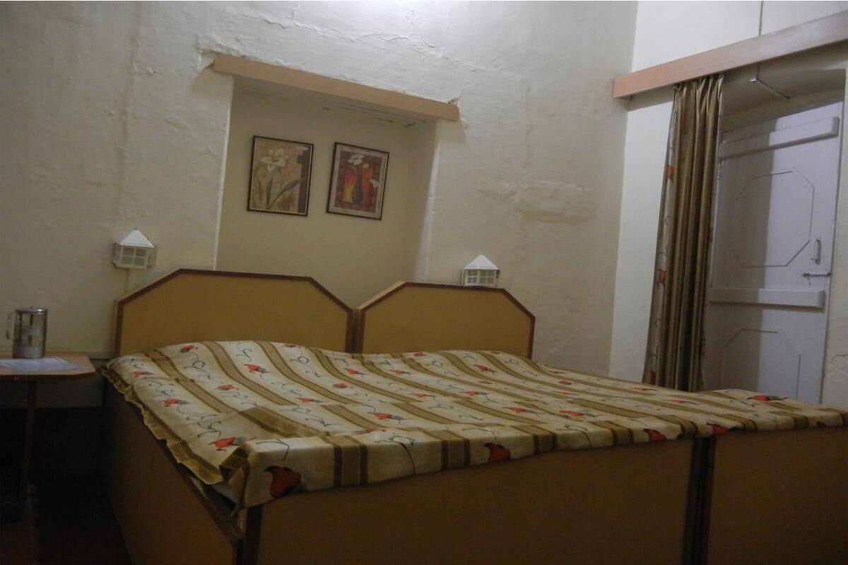 A bedroom with a bed, a nightstand, two wall-mounted lamps, and a door with curtains.