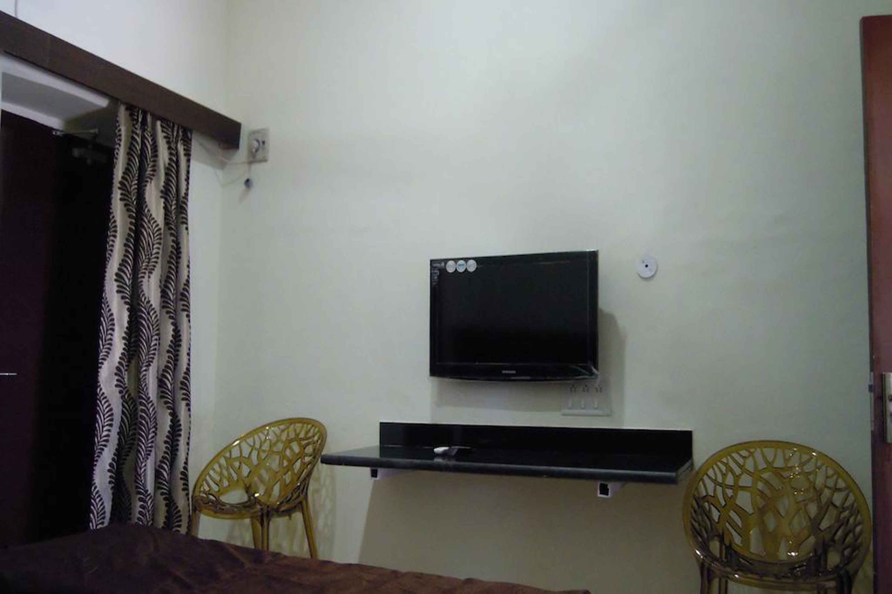 A bedroom with a bed, a television mounted on the wall, and two chairs.