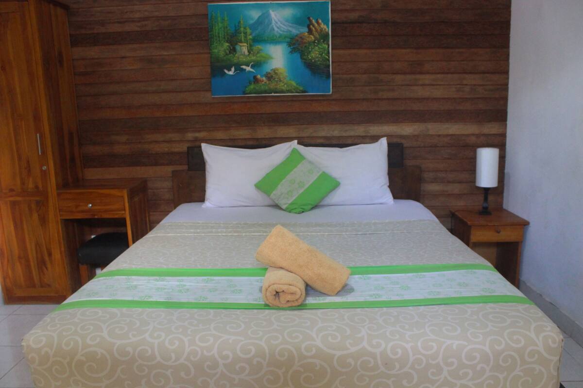 A neatly made bed with a green and white patterned bedspread, a rolled towel, and a pillow with a green accent.