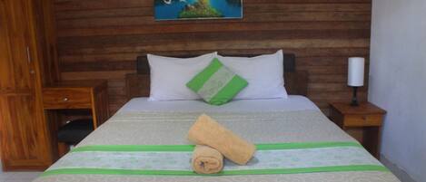 Una cama bien hecha con una colcha verde y blanca estampada, una toalla enrollada y un almohadón con detalles verdes.