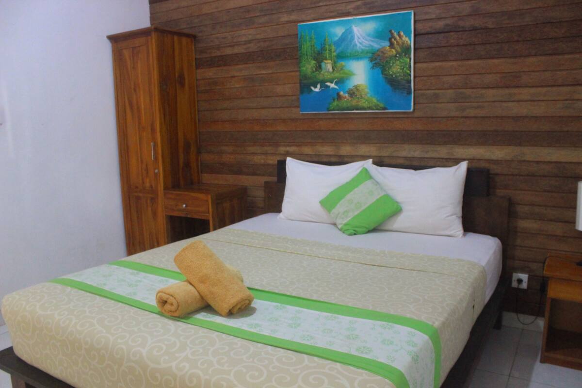 A neatly made bed with a green and white bedspread, a rolled towel, and a pillow with a green accent.
