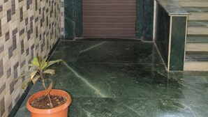 A lobby with a patterned tile wall, a potted plant, a door with a warning sign, and a marble floor. - Hotel Cool Palace (Nashik)