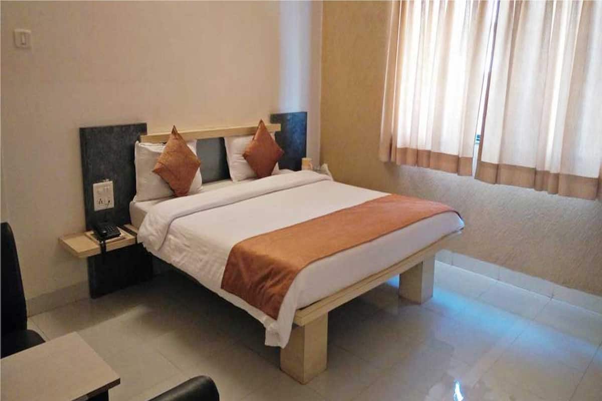 A neatly made bed with a white and brown bedspread, a bedside table with a phone, and a window with curtains.
