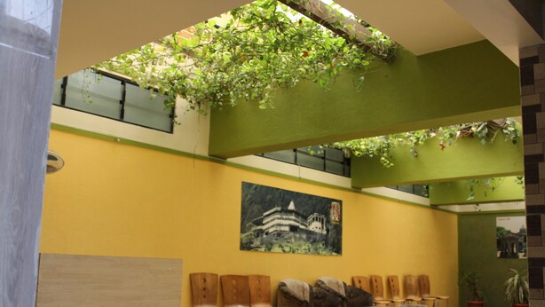 A lobby with a green and yellow color scheme, wooden chairs, a table, and a large painting on the wall. - Hotel Cool Palace (Nashik)