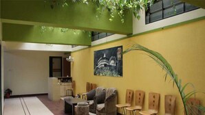 A lobby with a yellow wall, a painting, a reception desk, seating area, and a staircase. - Hotel Cool Palace (Nashik)