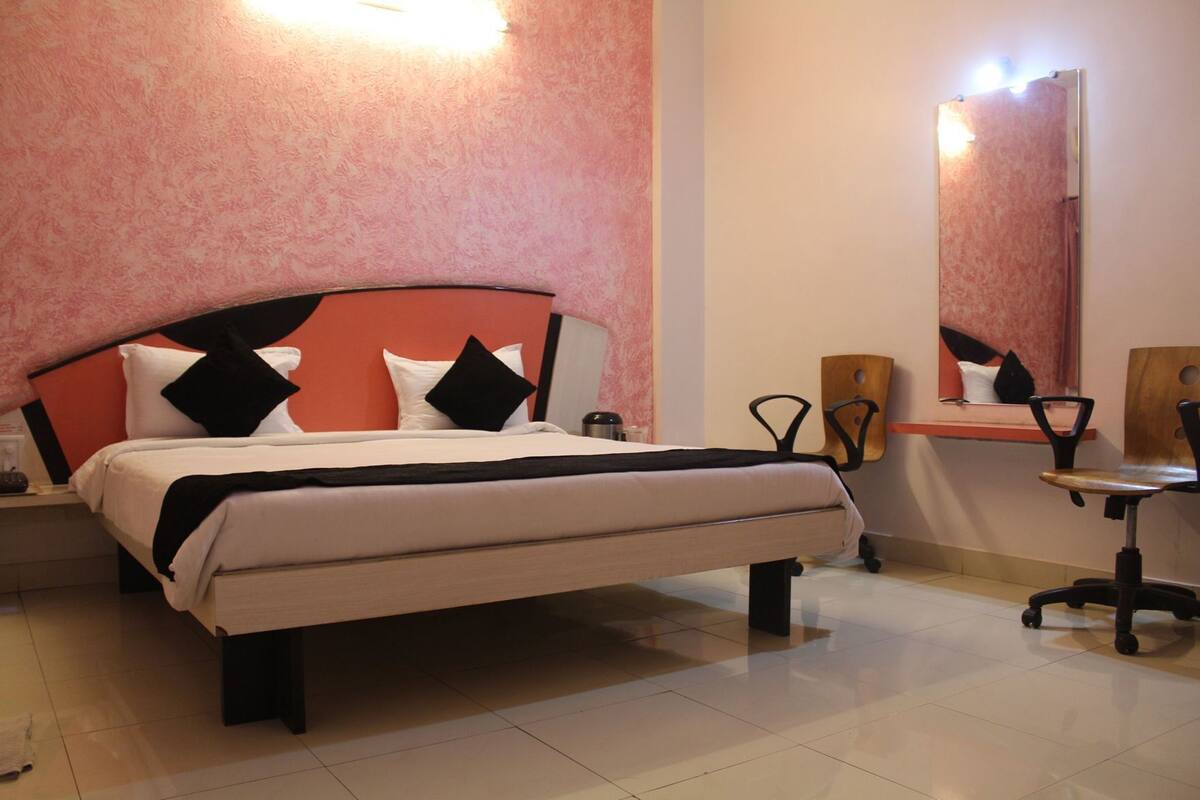 A hotel room with a bed, bedside table, chair, desk, and mirror.