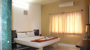 A hotel room with a bed, bedside table, and a window with curtains. - Hotel Cool Palace (Nashik)