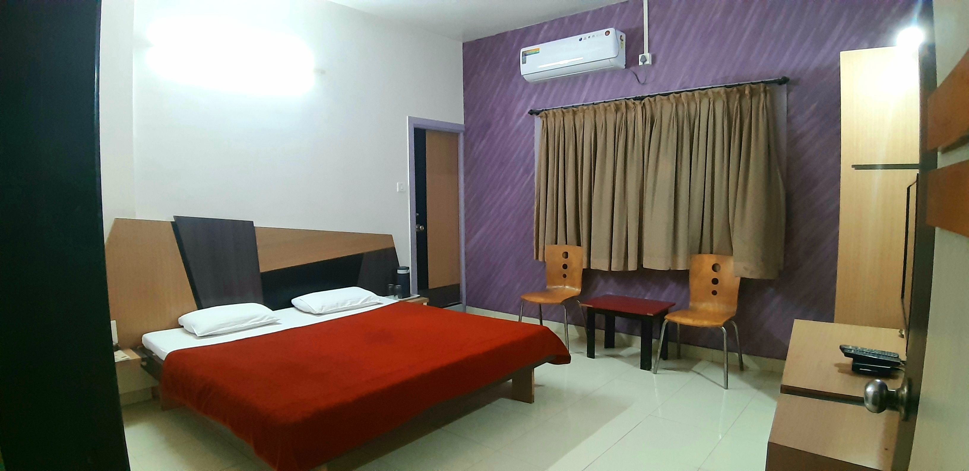 Una habitación con cama, dos sillas, una mesita, aire acondicionado y una puerta.