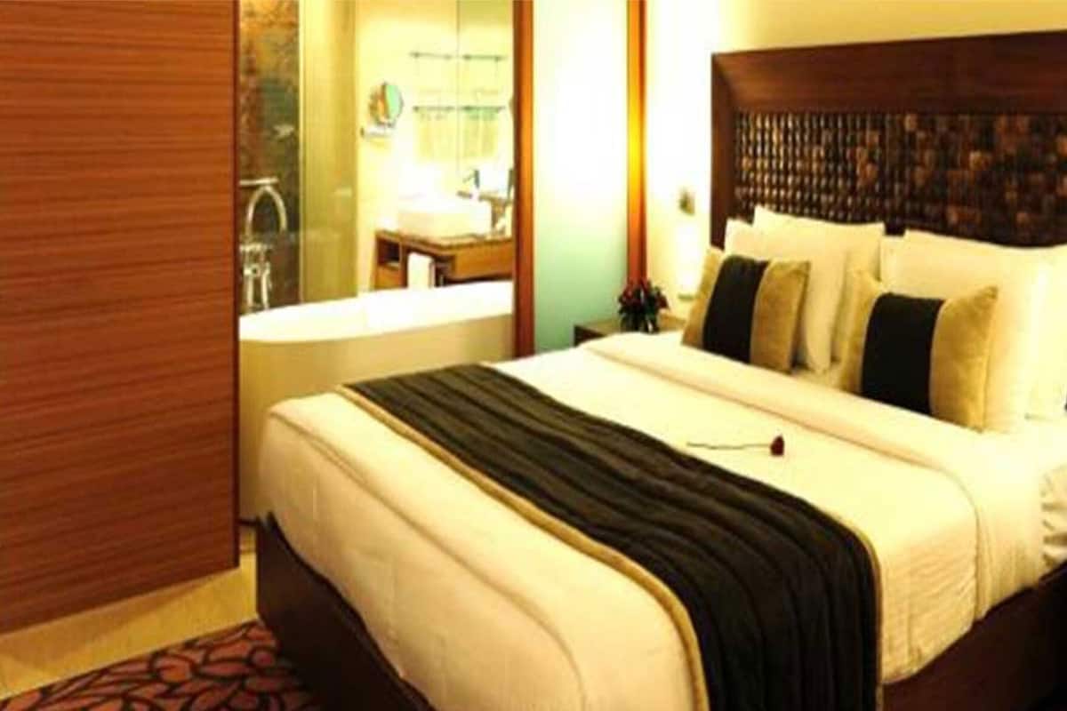 A hotel room with a large bed, a wooden headboard, a nightstand, and a bathroom visible in the background.