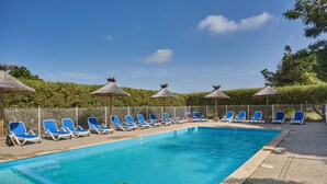 Une piscine bordée de chaises longues bleues et ombragée par des parasols en chaume.