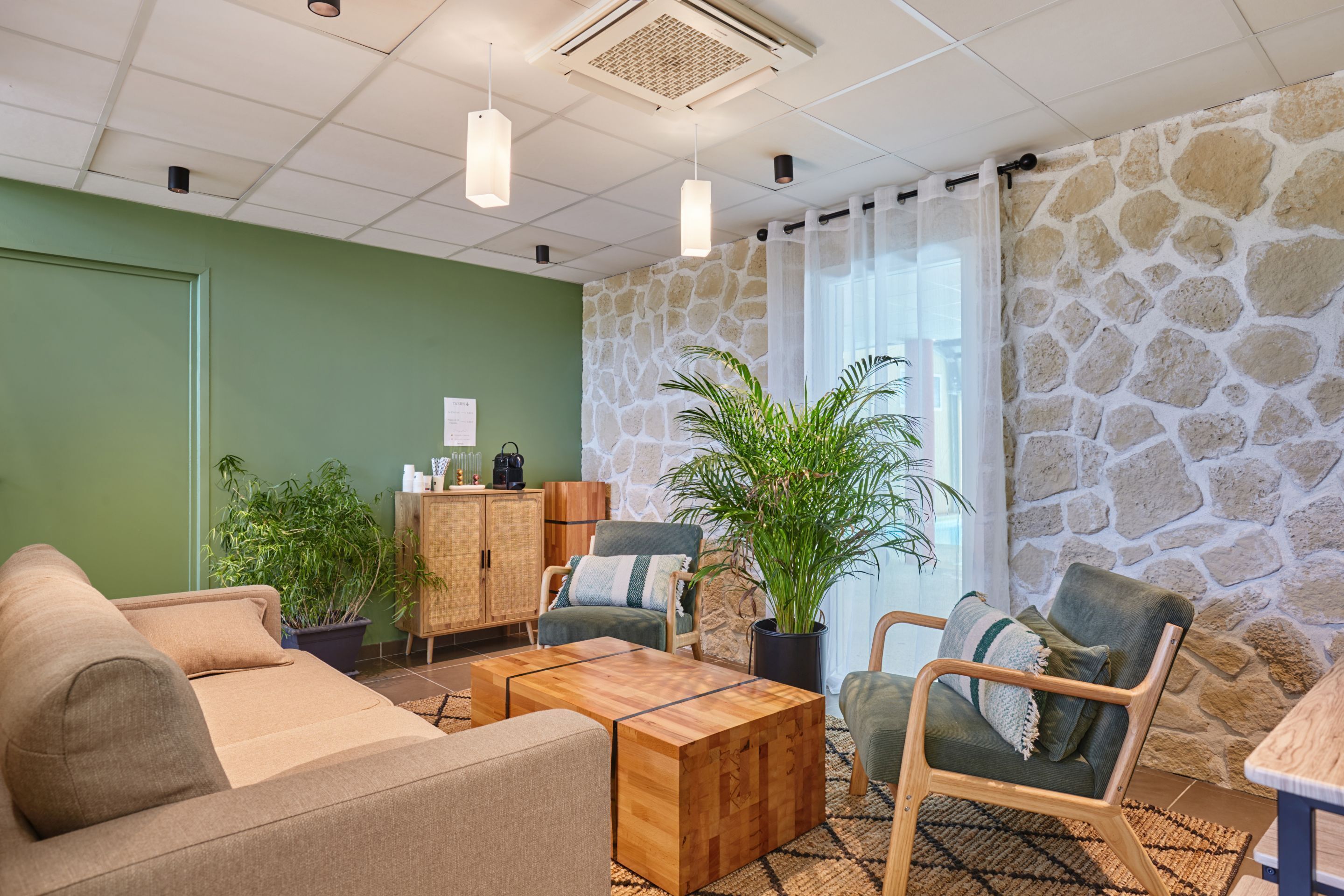 Un salon chaleureux avec un mur vert, un mur en pierre et une table basse en bois. On y trouve deux canapés, un meuble et une plante en pot.